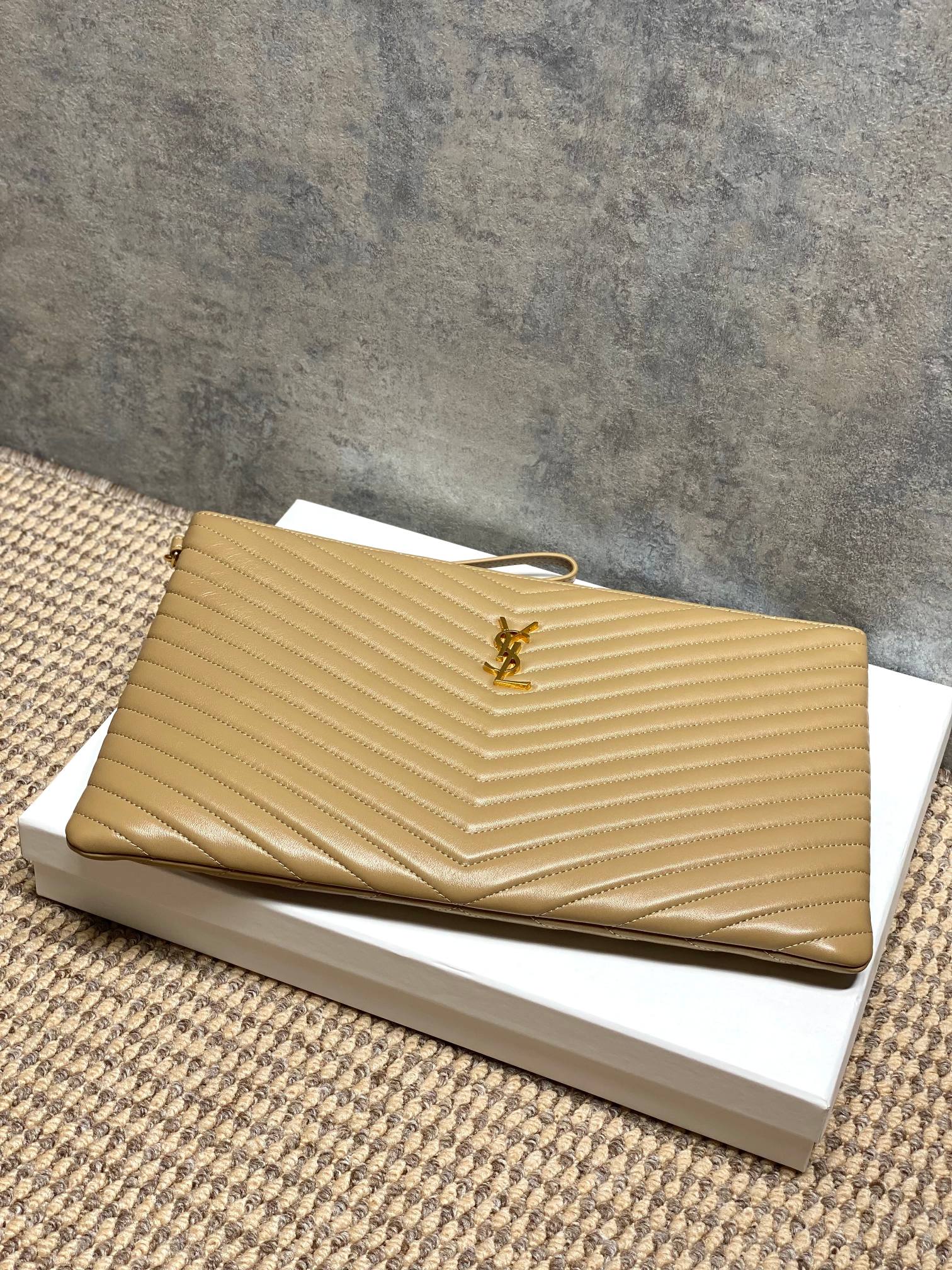 Gold tone quilted clutch bag with chevron pattern and central logo medallion