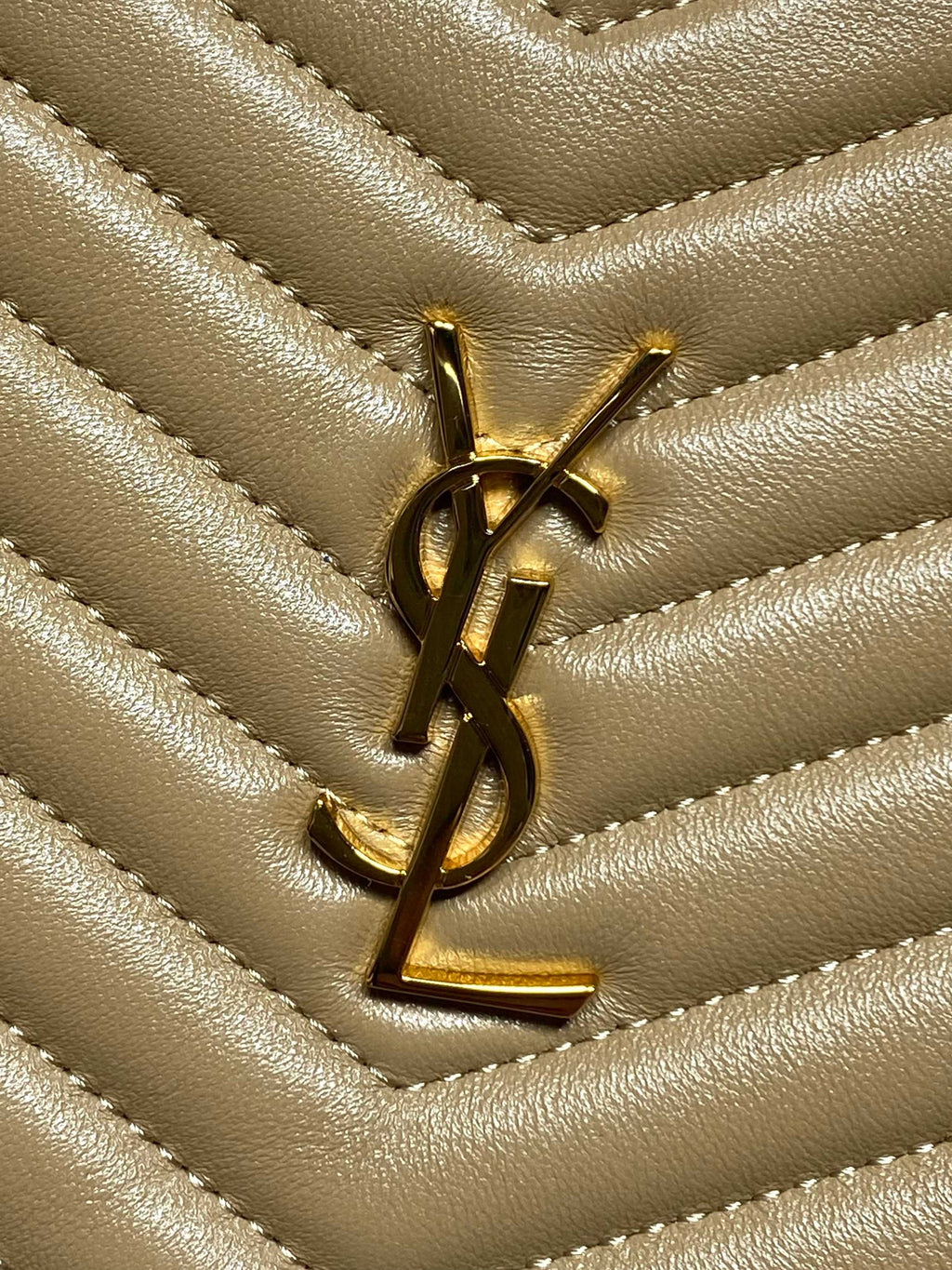 Gold YSL logo on chevron quilted leather small bag, close-up of emblem.