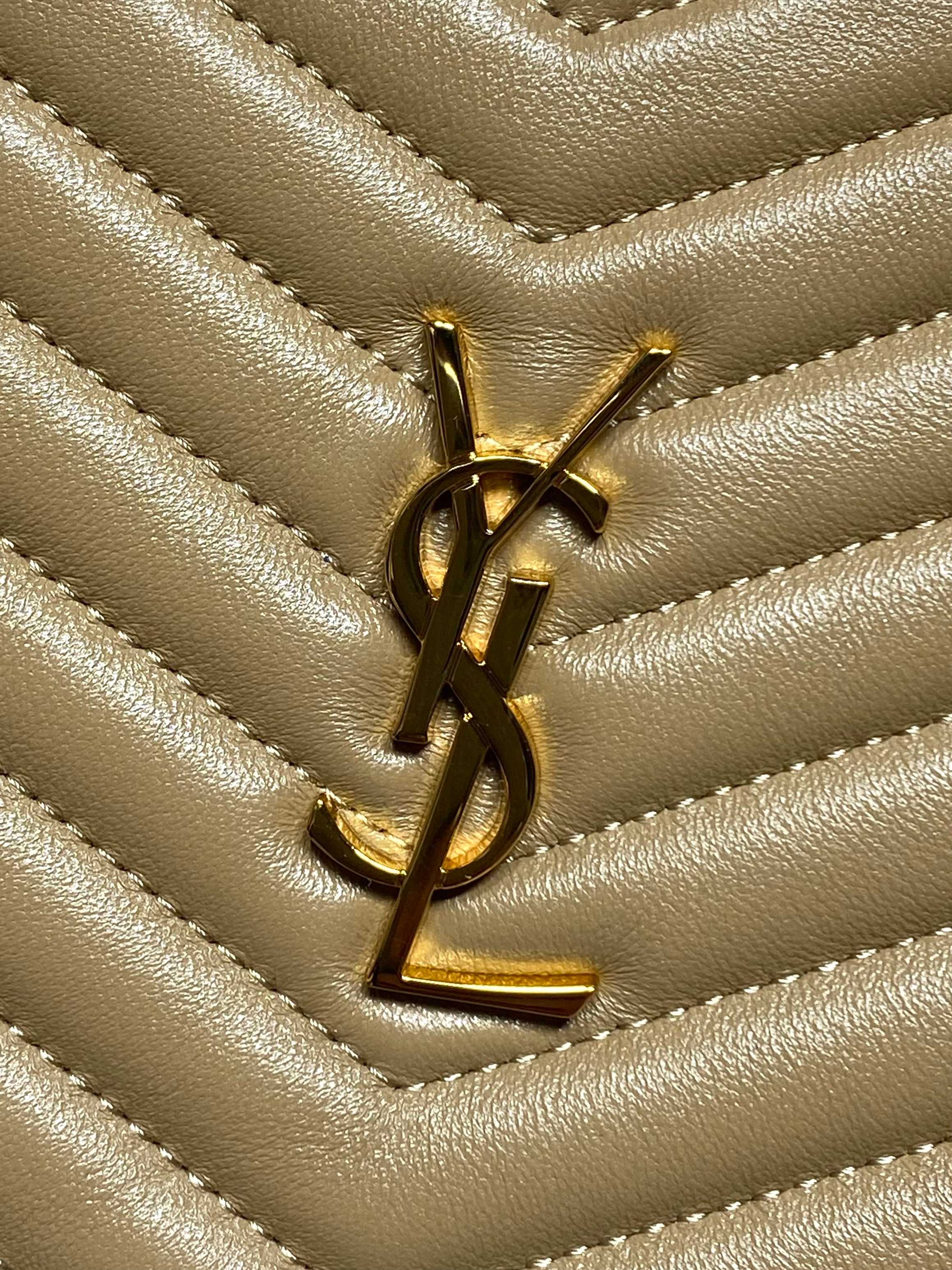 Gold YSL logo on chevron quilted leather small bag, close-up of emblem.