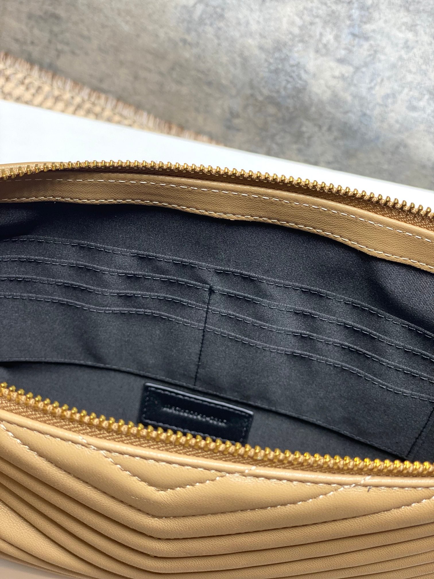 Inner pocket and dark lining inside tan quilted small bag with gold zipper