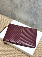 YSL quilted clutch bag in burgundy with gold YSL logo and top zip closure.