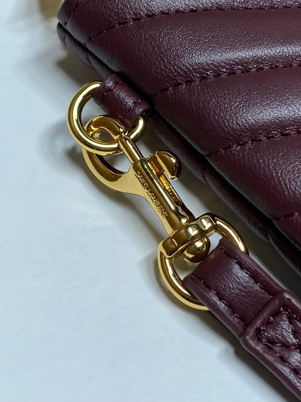 Close-up of gold keyring clasp and burgundy leather strap on YSL bag.