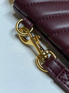 Close-up of gold keyring clasp and burgundy leather strap on YSL bag.