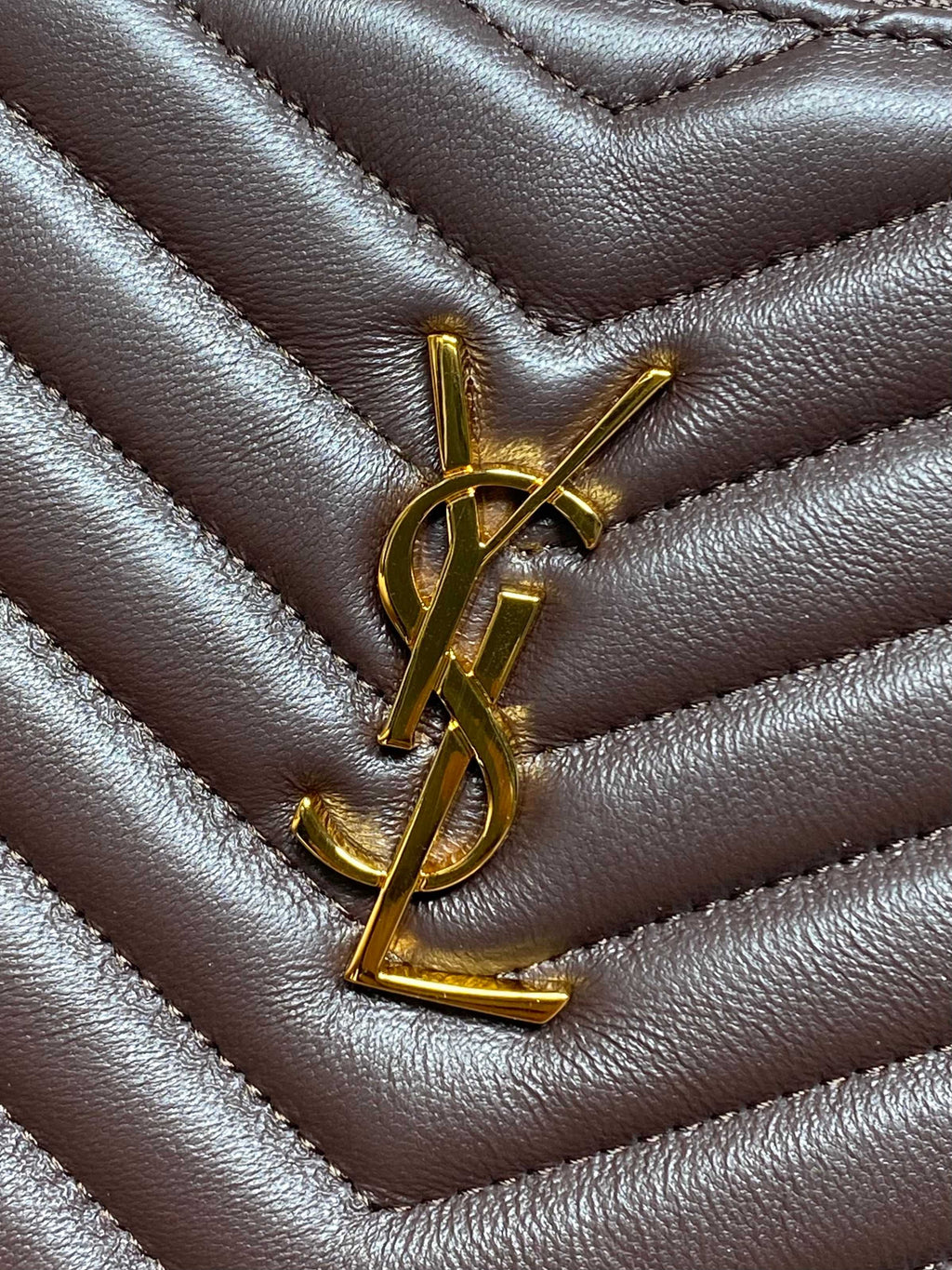 YSL logo charm on dark quilted leather bag with chevron stitching and gold hardware.