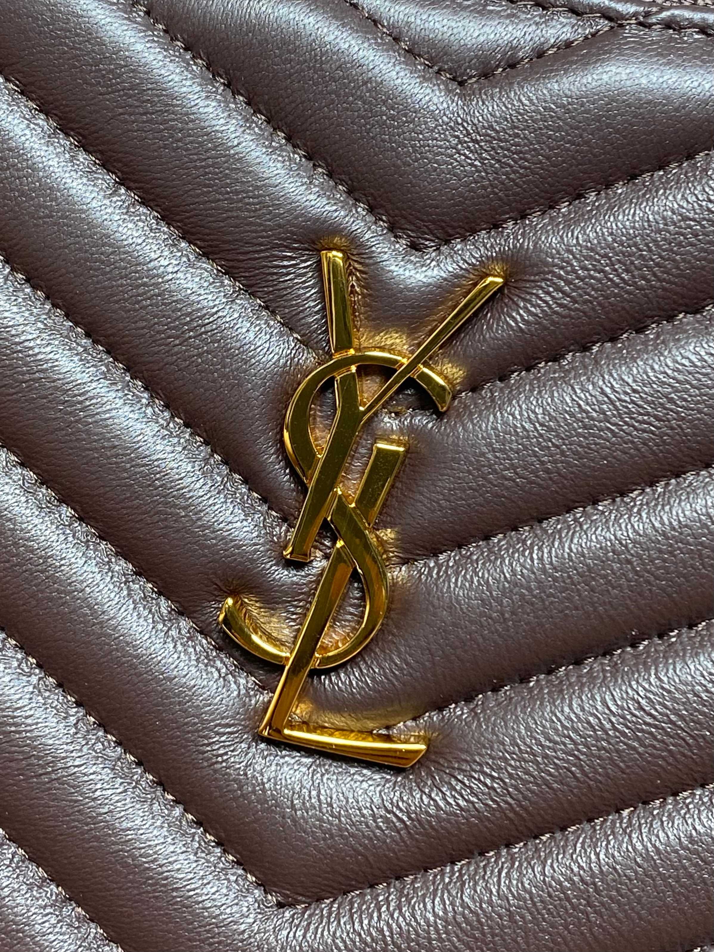 Close-up of gold YSL monogram on dark brown quilted leather bag