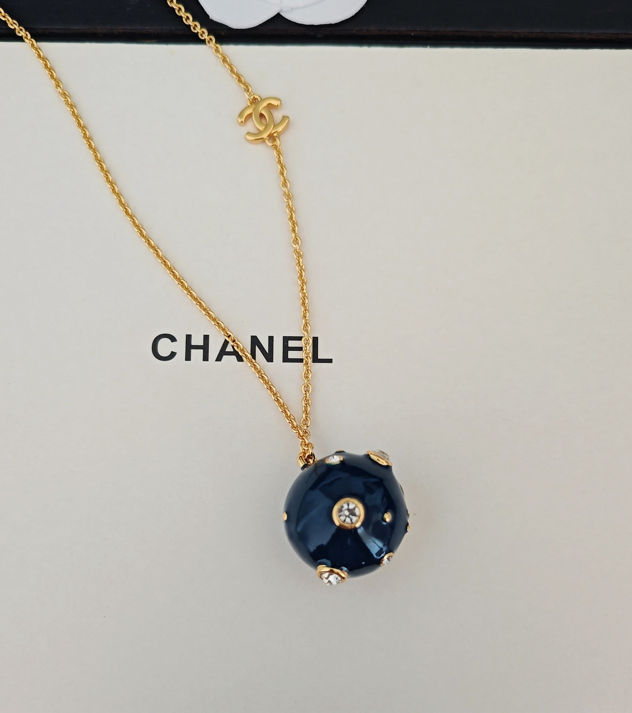 Gold-tone necklace with Chanel text and blue round crystal pendant