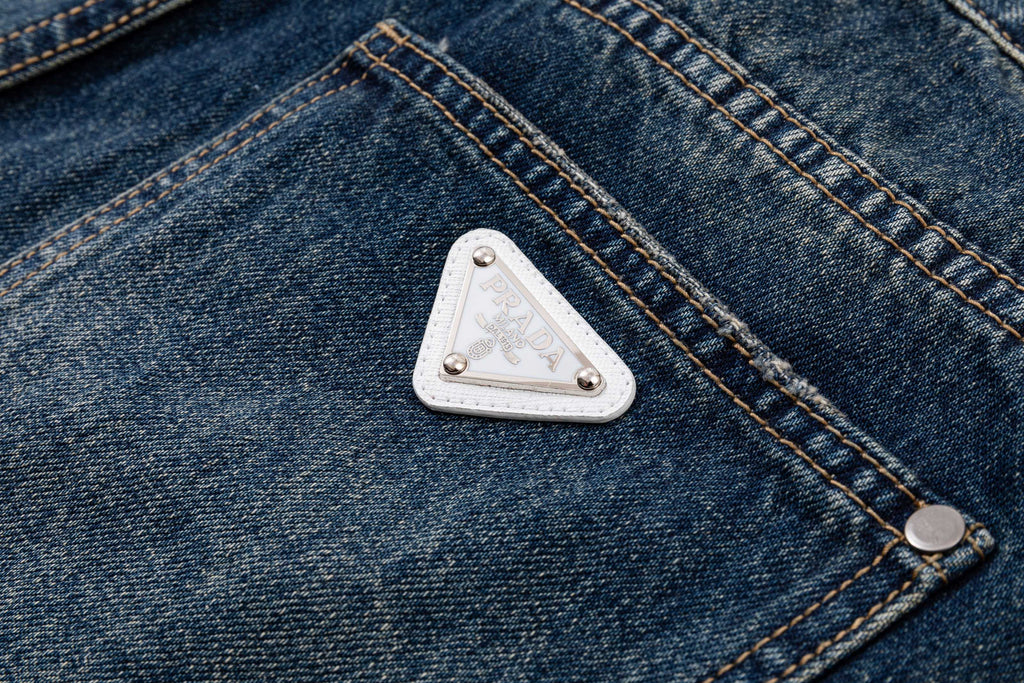 Prada denim pants pocket close-up with white triangle logo patch and buttons