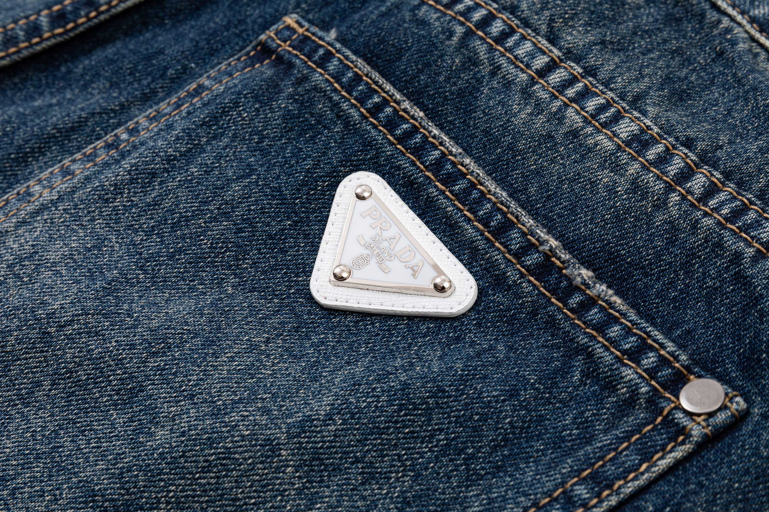 Prada denim pants pocket close-up with white triangle logo patch and buttons