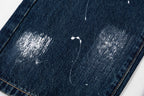 Dark blue denim pants with stitched hem and distressing spots, cropped close-up