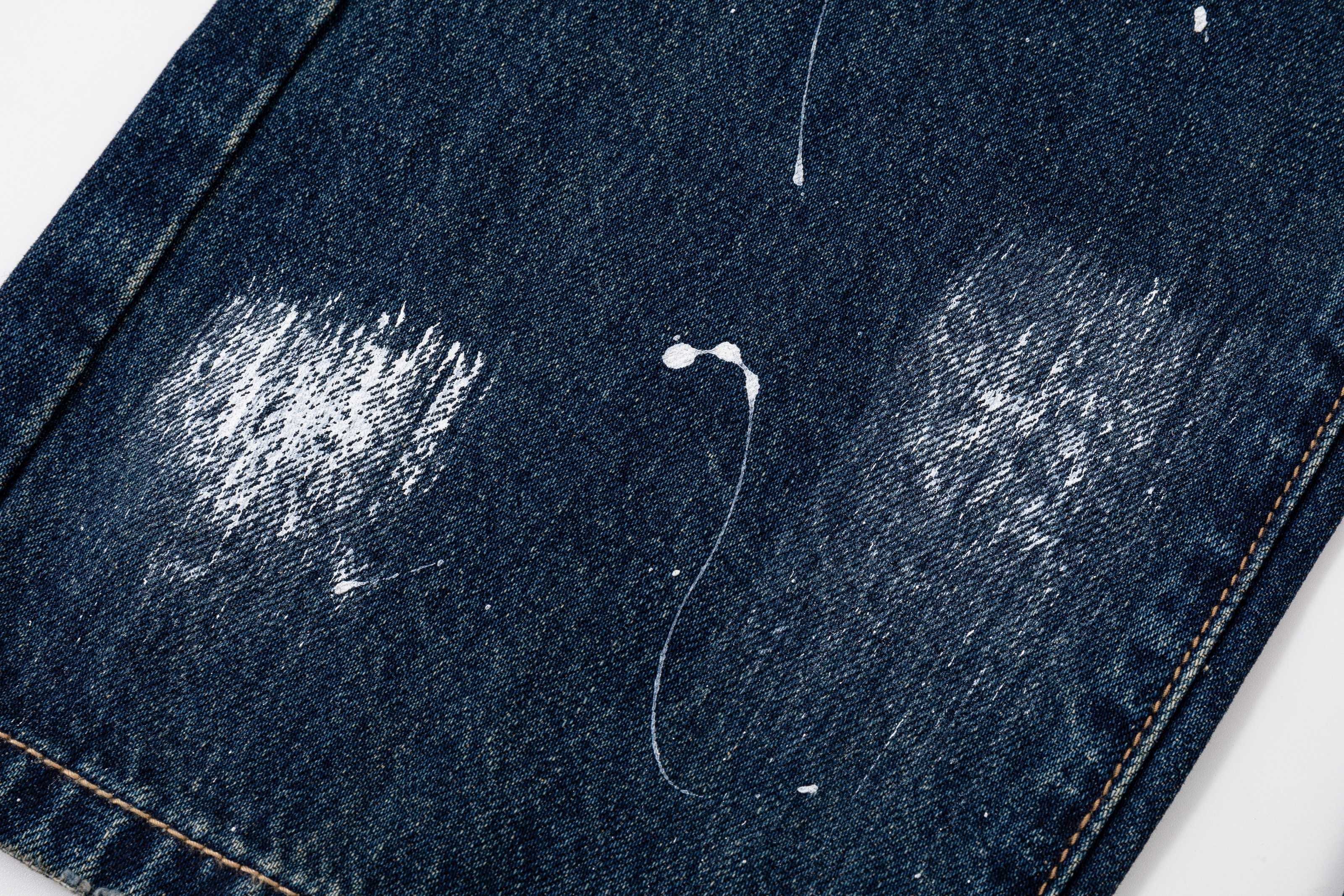 Dark blue denim pants with stitched hem and distressing spots, cropped close-up