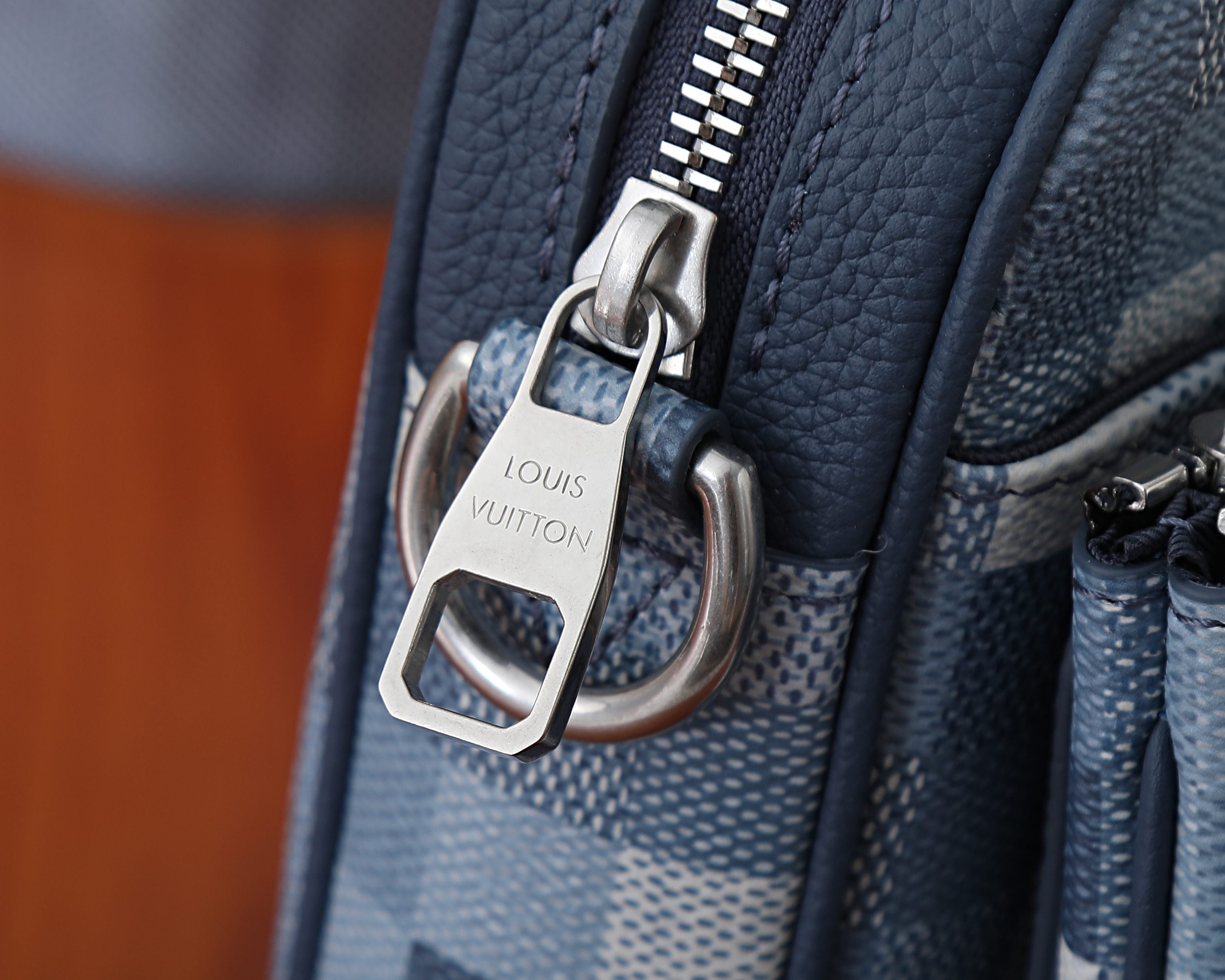 Crossbody bag lock detail with metal tab and “LOUIS VUITTON” engraving.