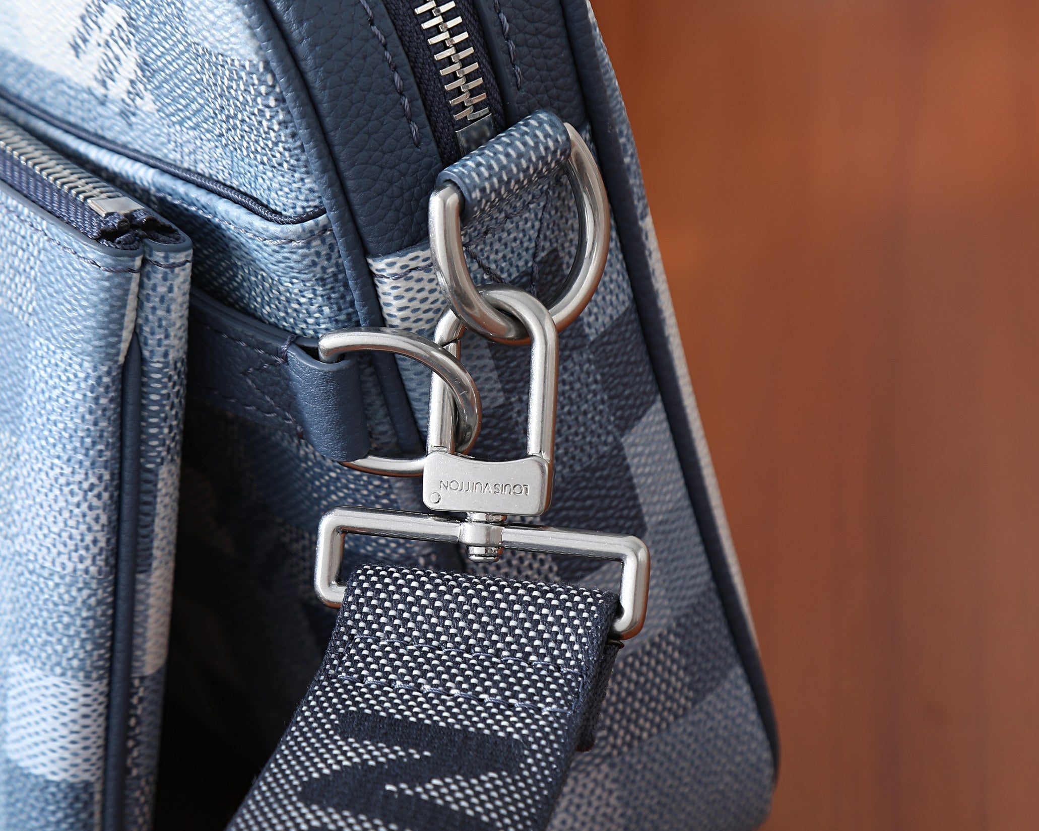 Crossbody bag hardware with metal D-rings, zipper pull, and blue checkered body.