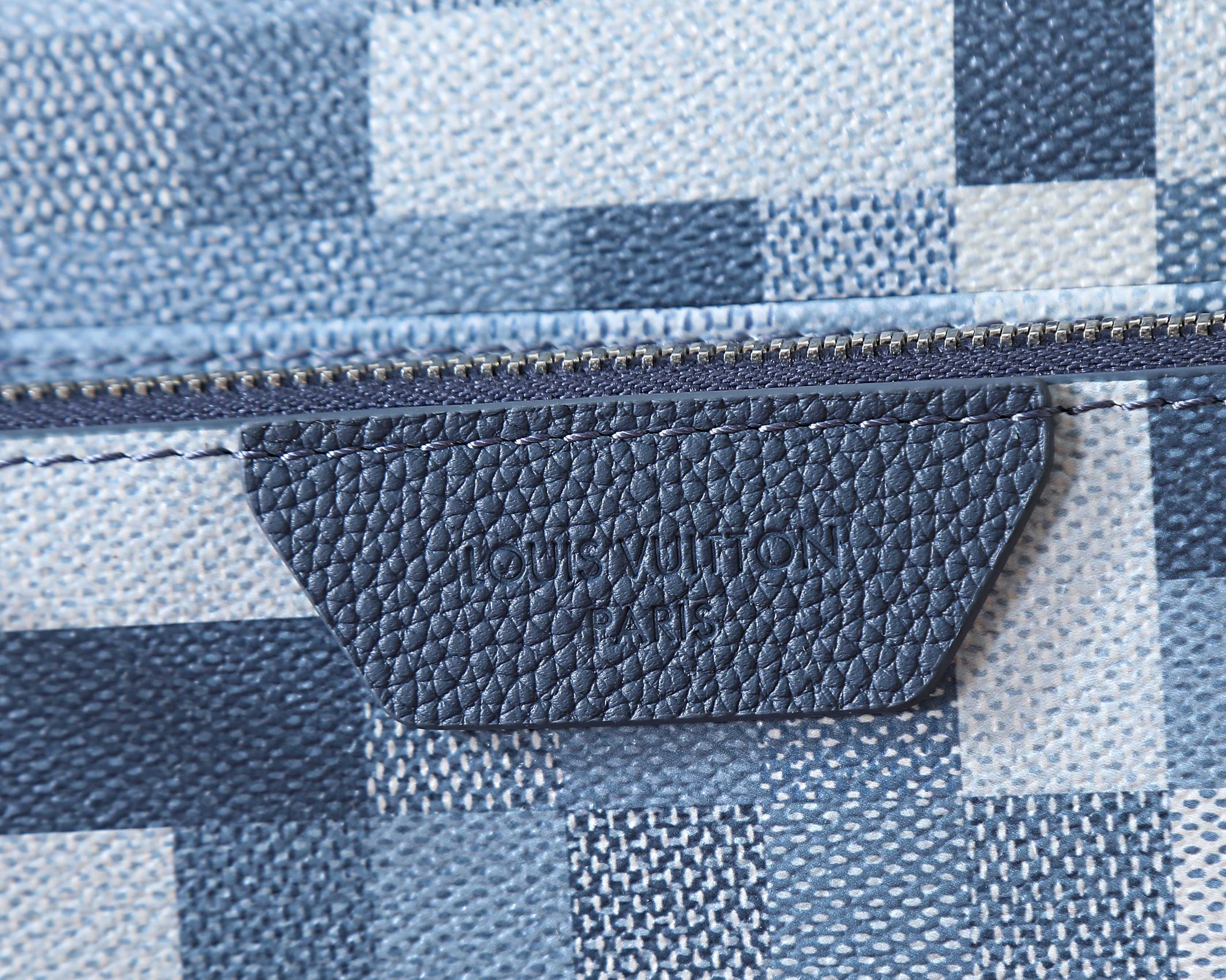 Crossbody bag interior label at zipper seam on blue and white checkered fabric.