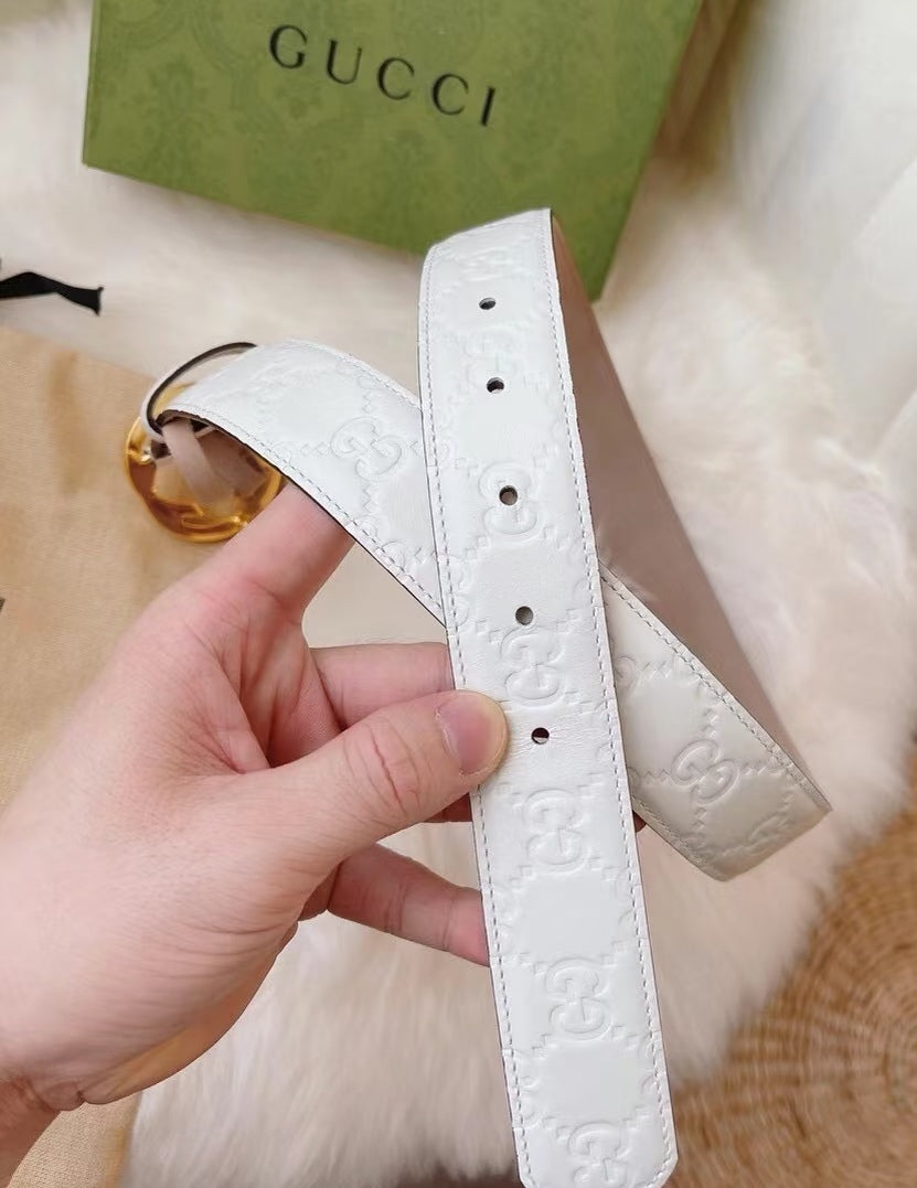Gucci belt strap close-up in white with embossed logo and gold buckle hardware