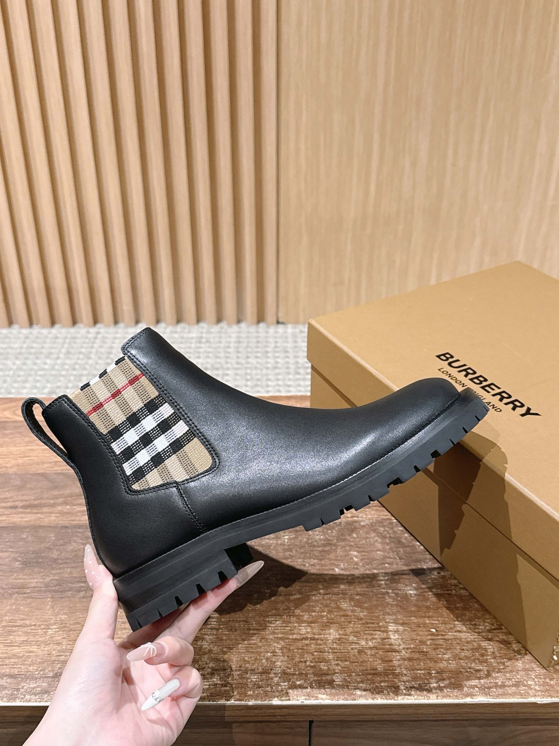 Black Chelsea boots with check-pattern elastic panel, held next to box