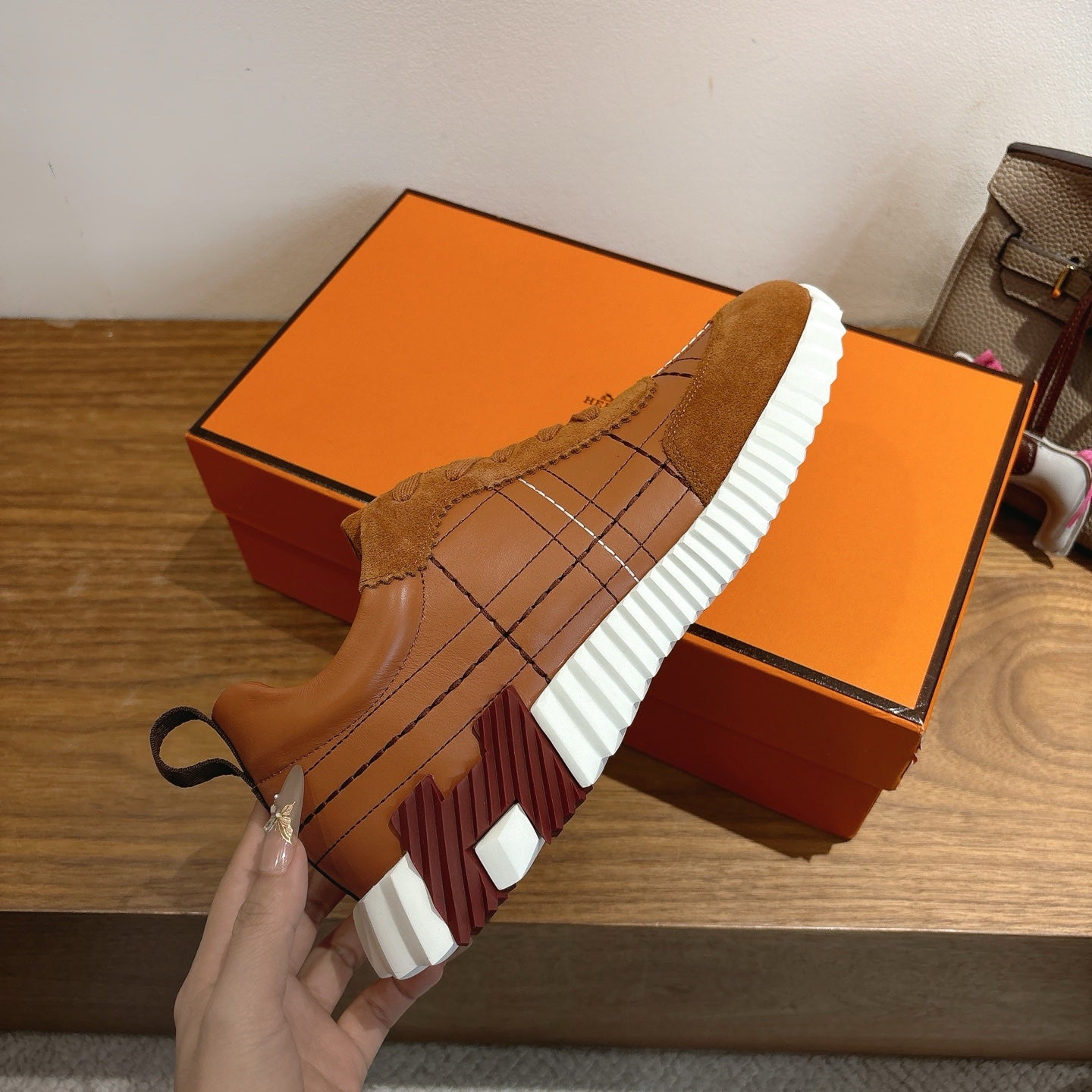 Hermes unisex sneakers heel view, brown suede upper with white striped sole tread.