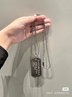 Silver-tone bead necklace with dog tag pendant held in hand