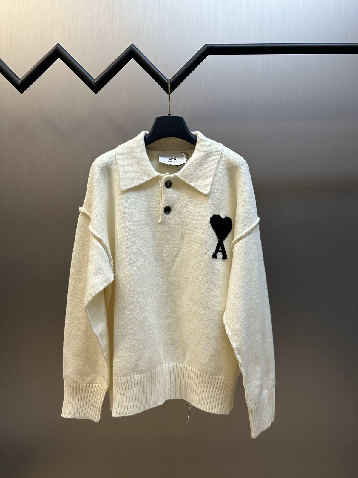 Off-white knit sweater with collared neckline, black button placket, heart and A logo