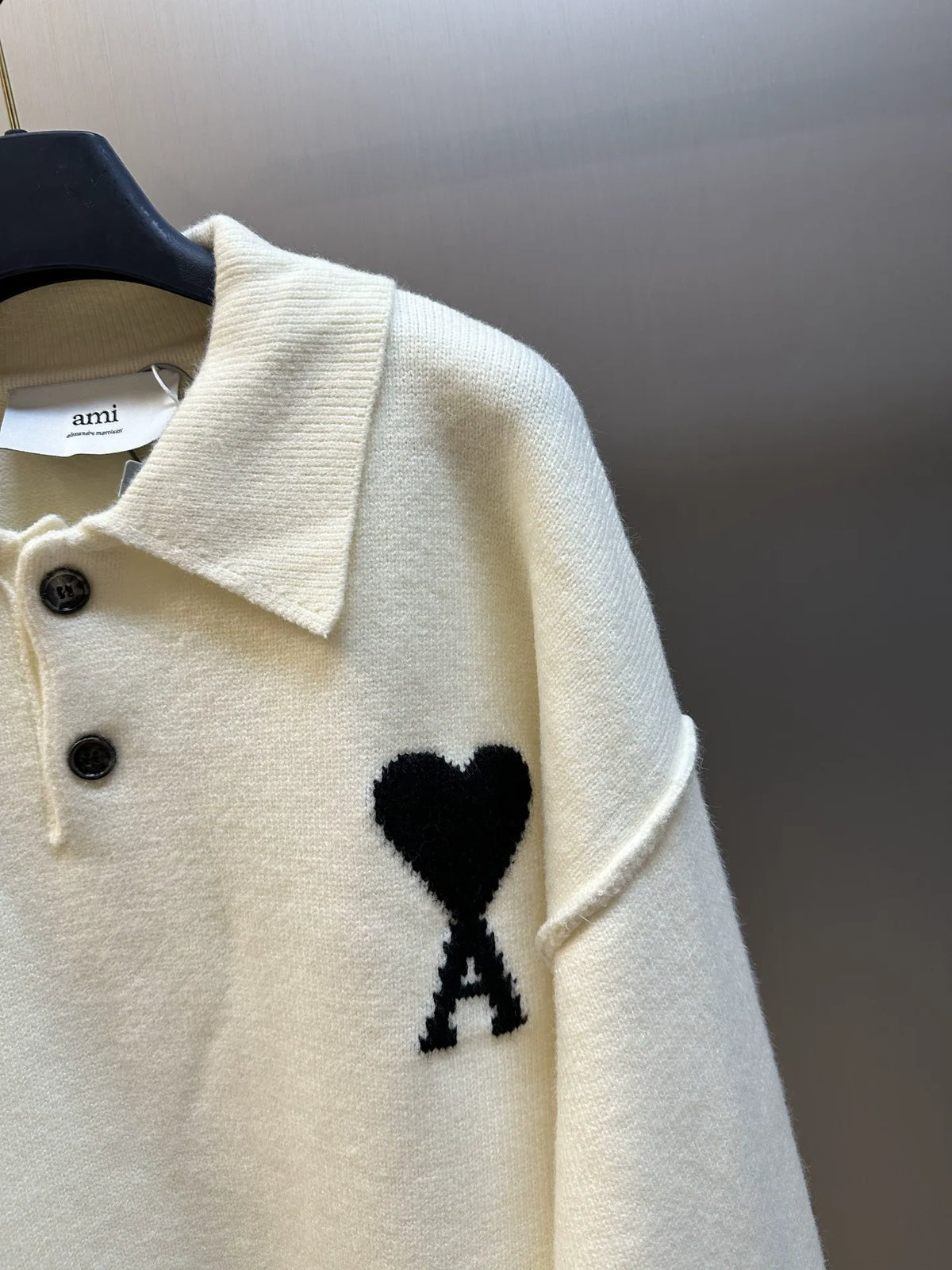 Off-white sweater close-up with collared knit, black buttons, heart with A patch