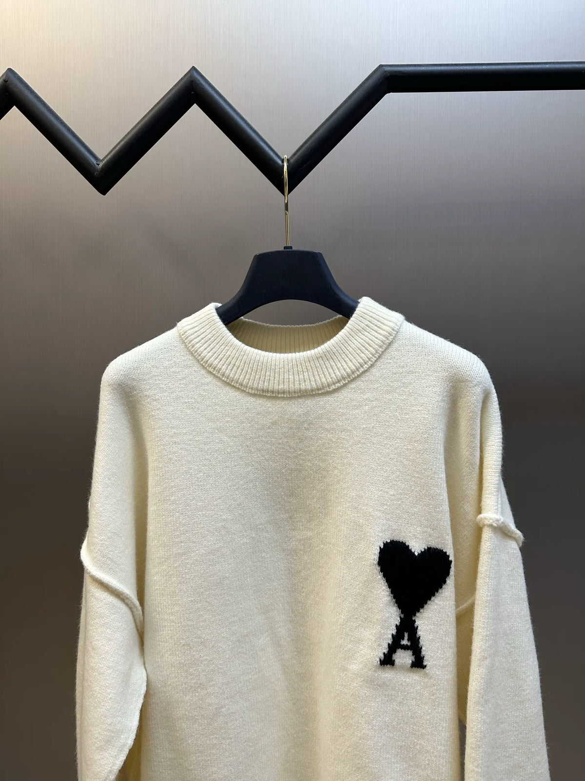 Amiri cream knit sweater on hanger with black heart-and-A logo patch