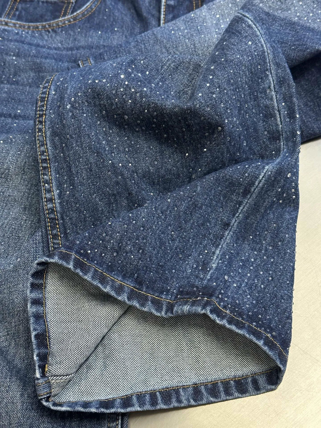 Dark blue denim jeans cuff with speckled texture and contrast-stitched hem.