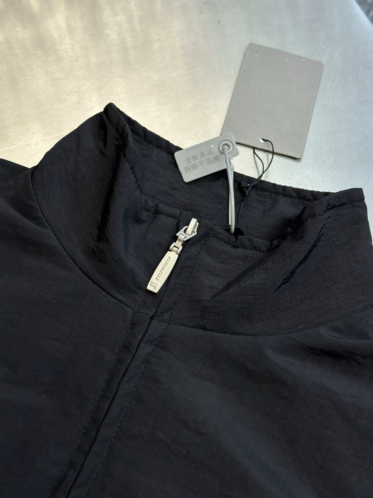 Black bomber jacket fabric close-up with zip pull and inner tag