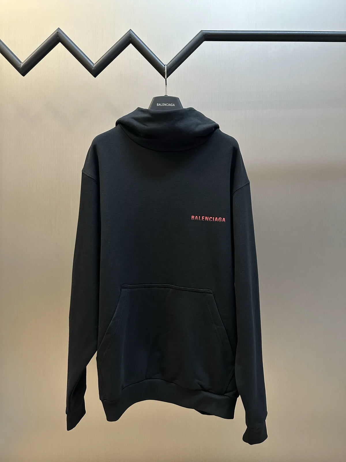 Black long-sleeve hoodie with hood, front pocket, and red BALENCIAGA logo
