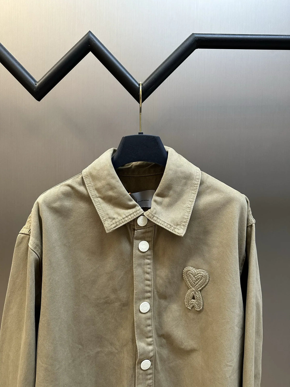 Light tan long-sleeve button-up jacket with pointed collar and embroidered heart emblem