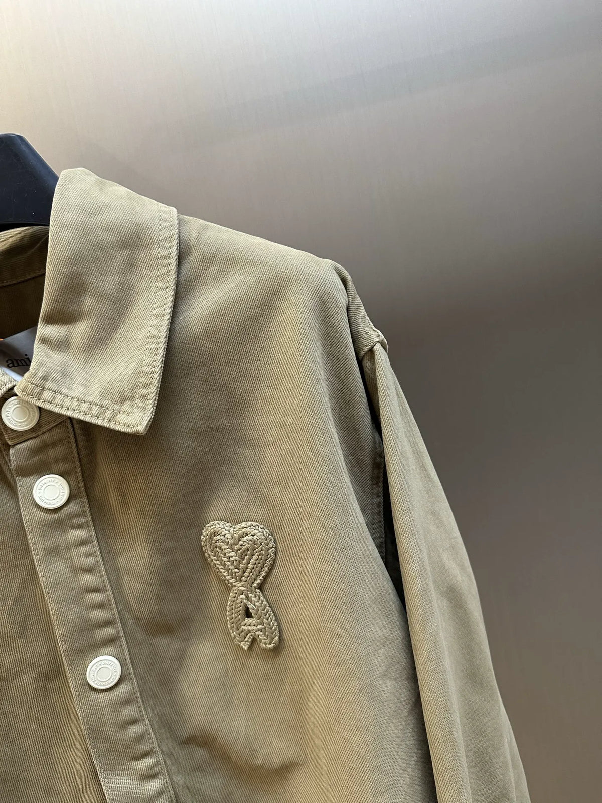 Light tan long-sleeve button-up jacket with embroidered heart emblem on chest