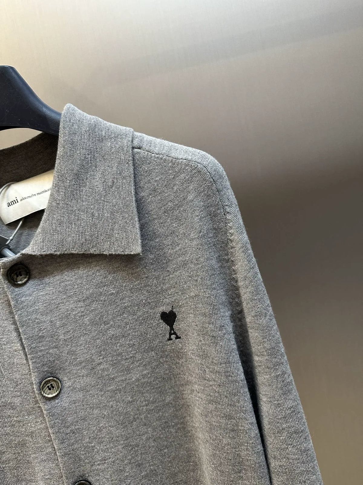 Gray knit polo top with button front, pointed collar, and small black bear icon