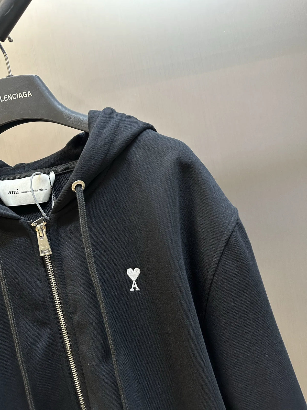 Black zip-up hoodie with hood and heart-and-A emblem on the chest