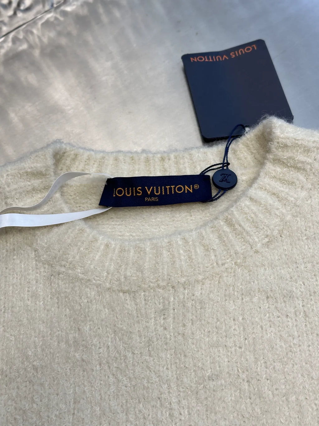 Off-white crewneck knit sweater with blue Louis Vuitton-style neck tag detail