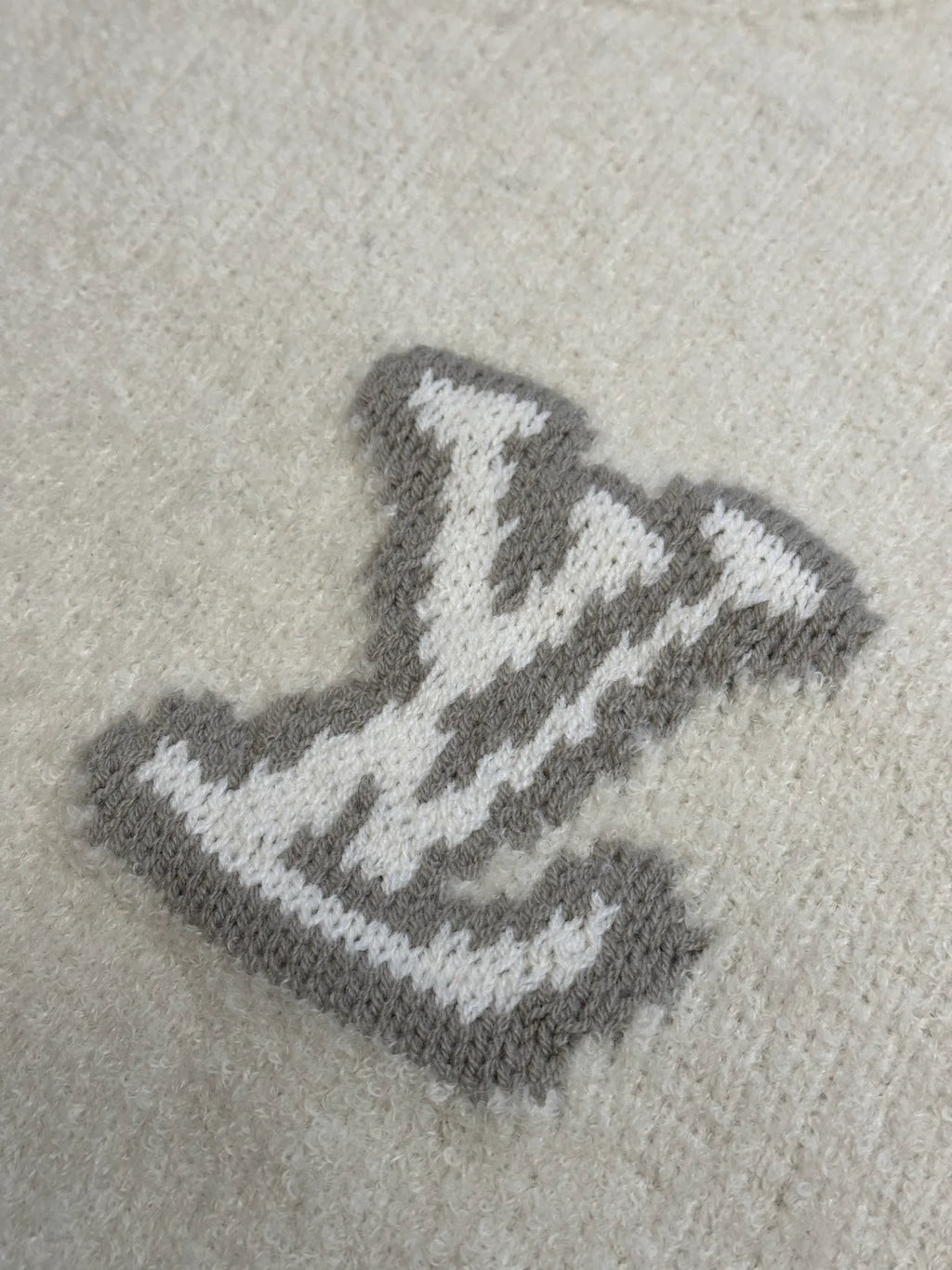 Close-up of LV-style monogram embroidery on off-white knit sweater