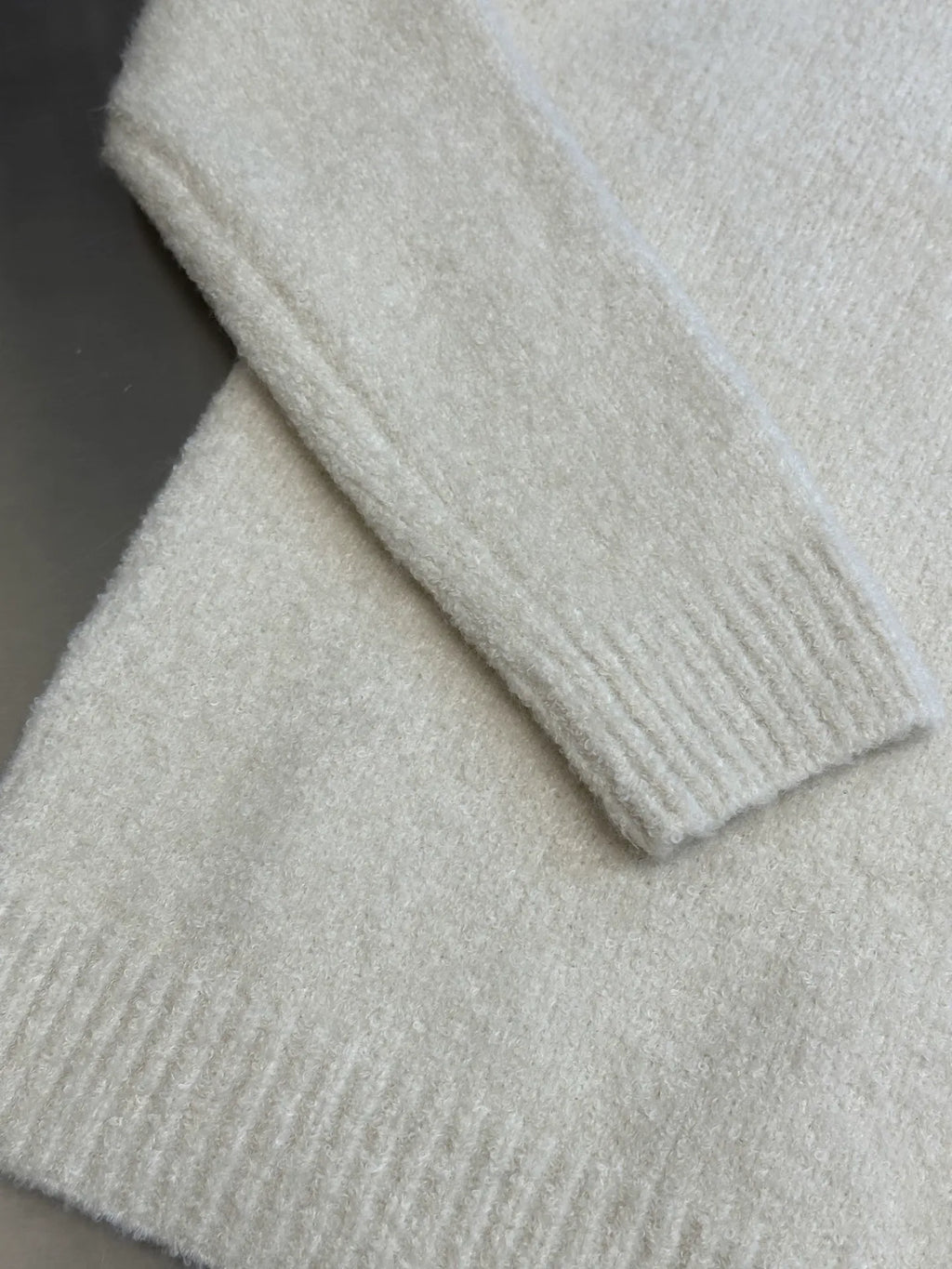 Off-white knit sweater sleeve cuff with ribbed trim and soft textured fabric