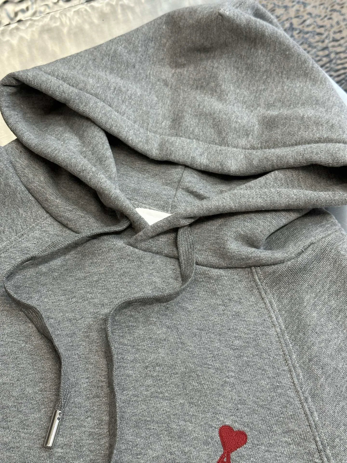 Heather gray hoodie close-up showing hood, drawcords, kangaroo pocket, and red logo