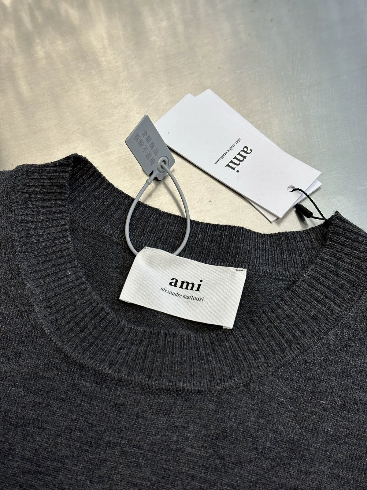 Dark gray crewneck sweater with ribbed neckline; tags hanging from the collar
