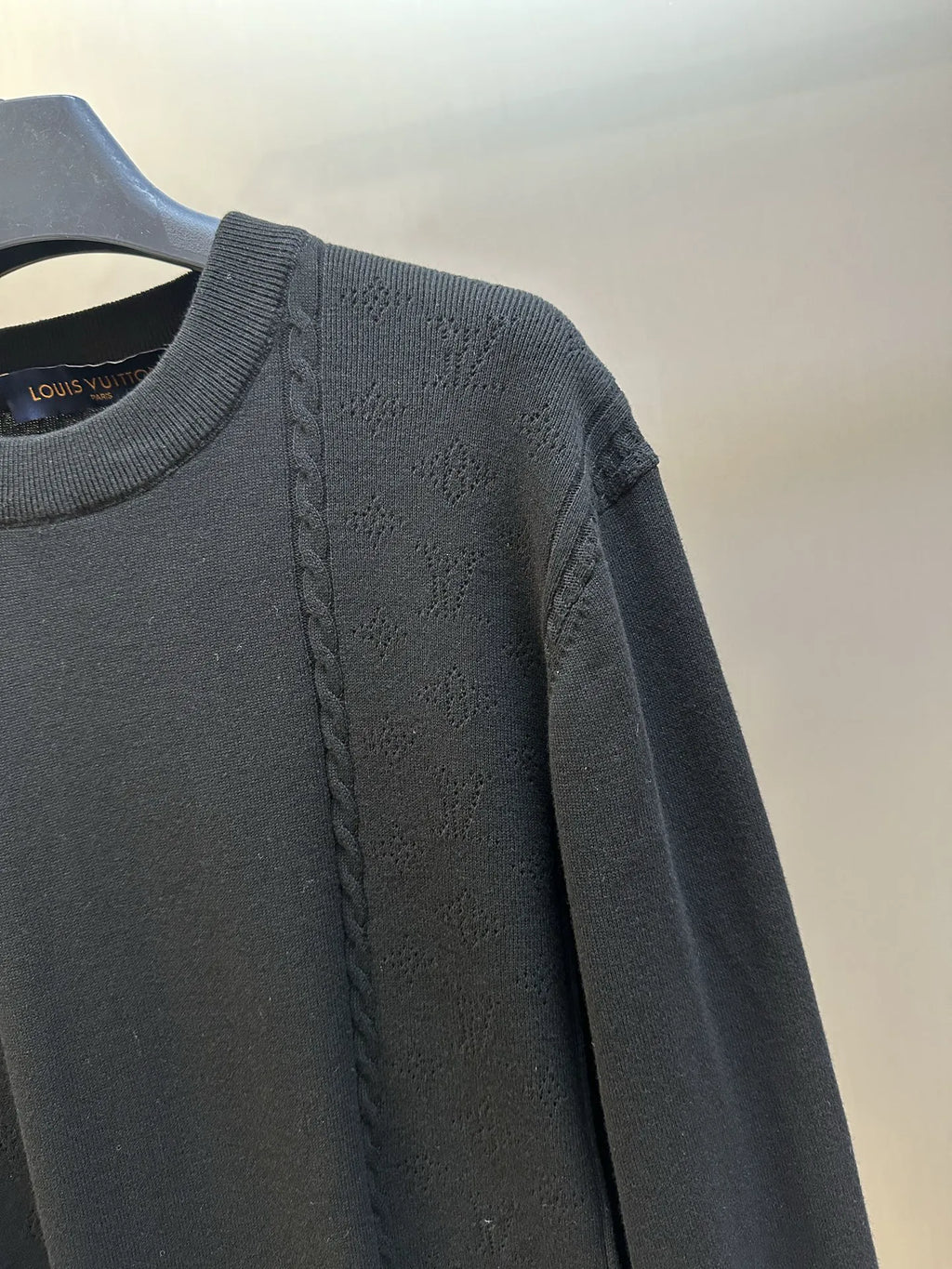 Black long-sleeve sweater with braided cable detail along the shoulder