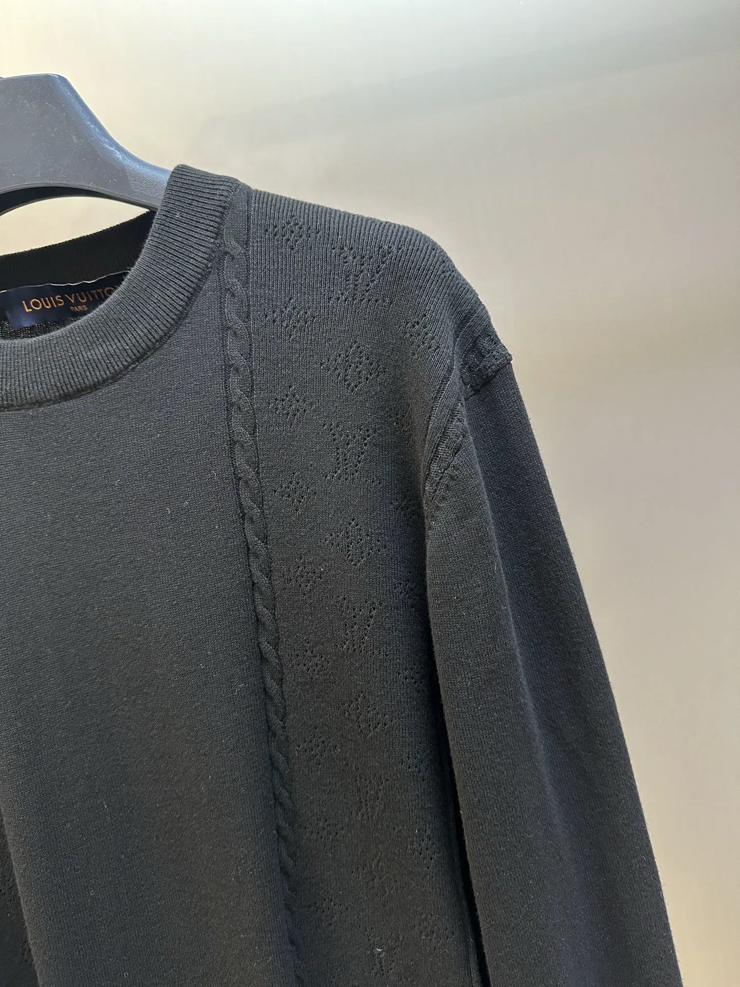 Black long-sleeve sweater with braided cable detail along the shoulder