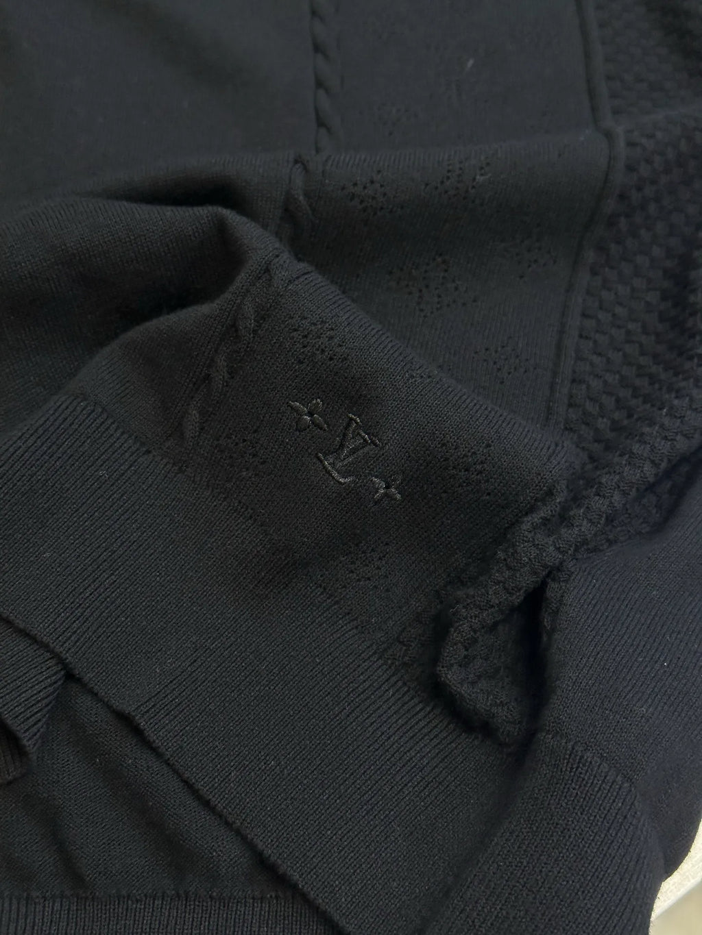 Black long-sleeve sweater with small stitched emblem on knit panel