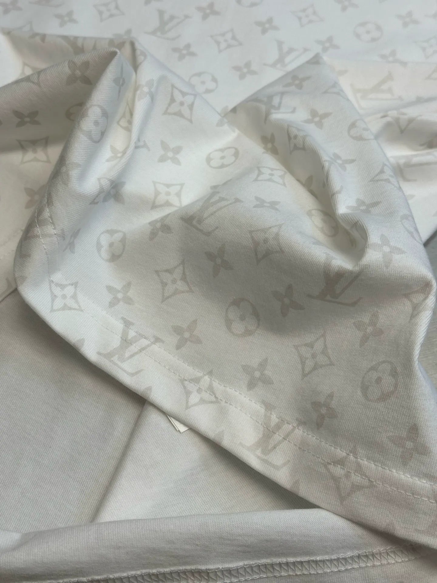Light-colored T-shirt fabric with repeating monogram pattern, close-up fold