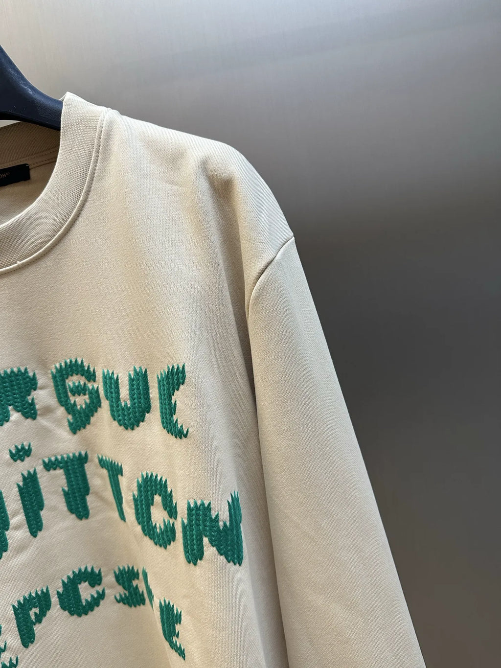 Cream sweatshirt sleeve and partial green graphic lettering on front.