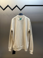 Cream long-sleeve sweatshirt, back view with small green logo patch near collar.