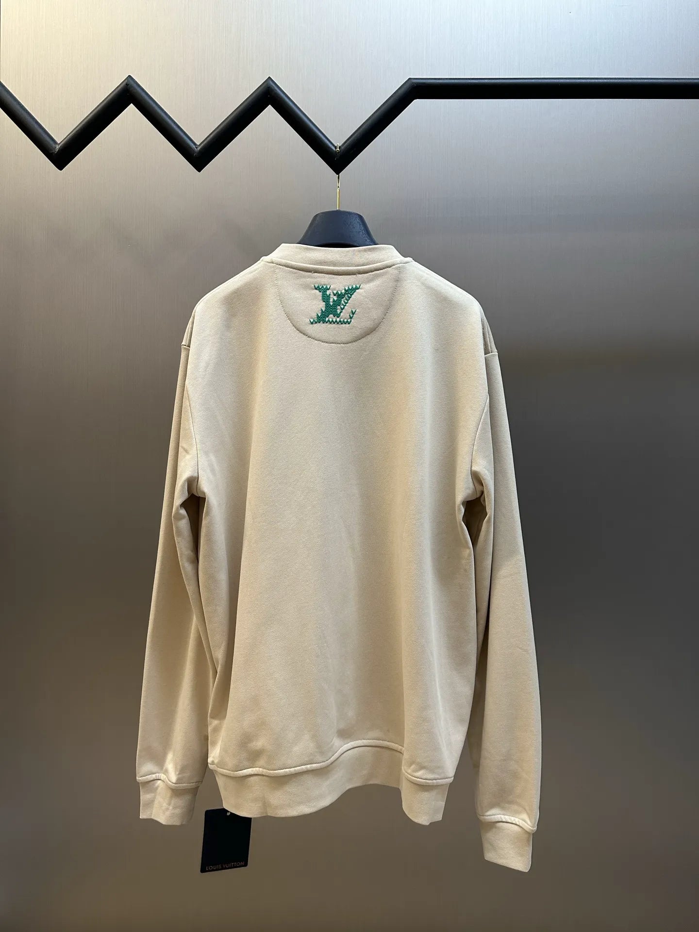 Cream long-sleeve sweatshirt, back view with small green logo patch near collar.