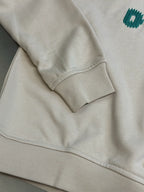 Cream long-sleeve sweatshirt with ribbed cuff and visible seam on sleeve.