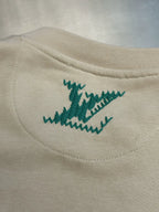 Cream sweatshirt with small green stitched logo on side chest near hem.