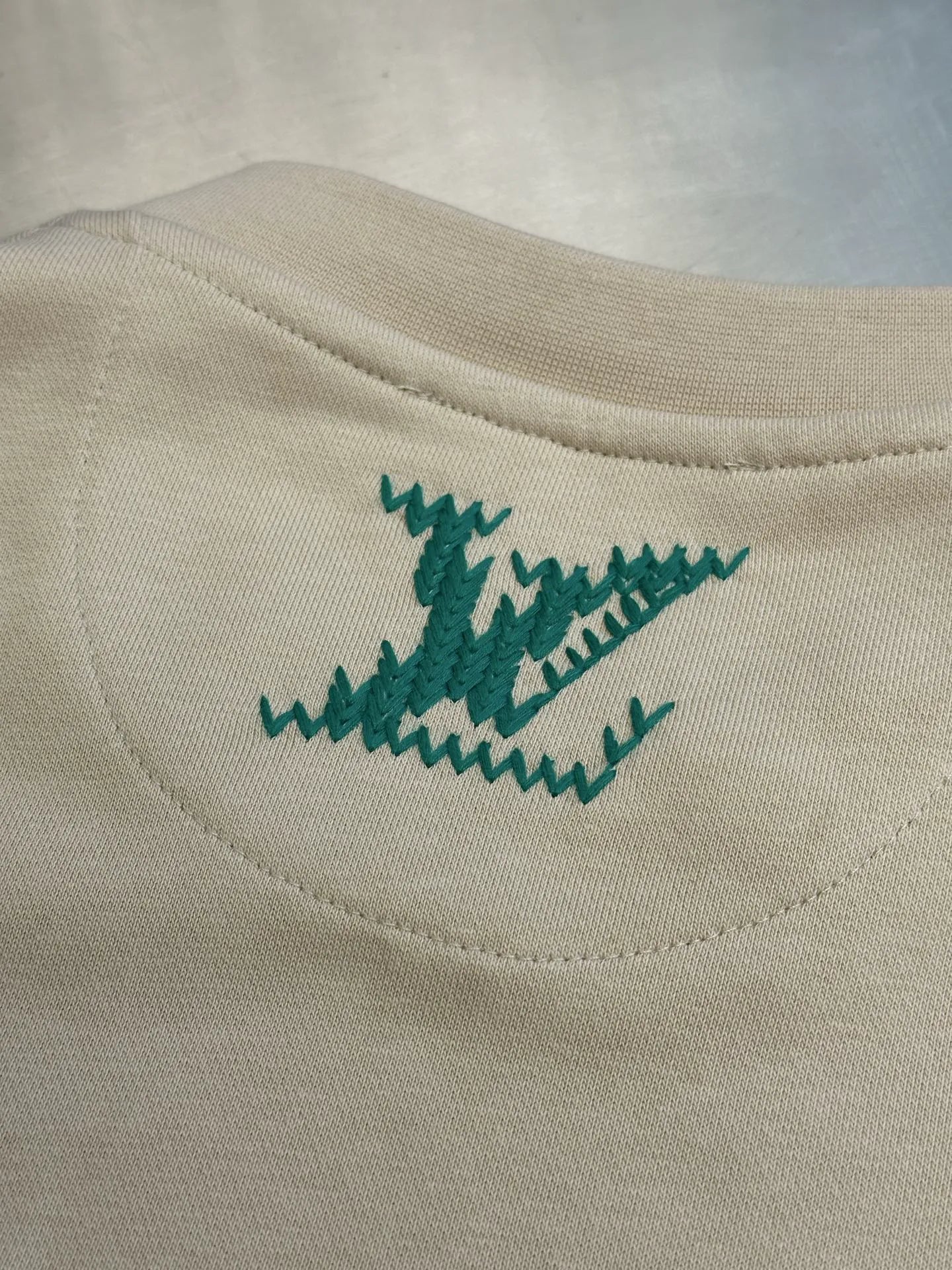 Cream sweatshirt with small green stitched logo on side chest near hem.