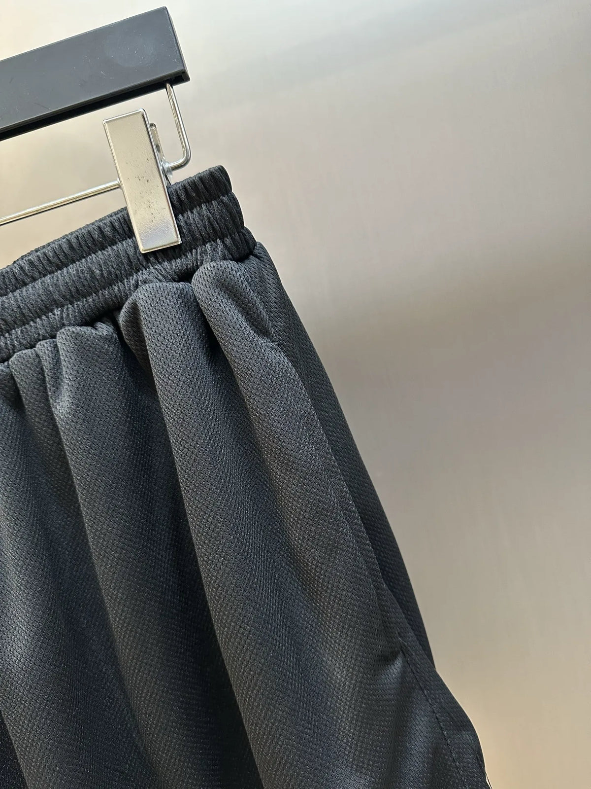 Black elastic-waist shorts, close-up of ribbed waistband and pleated fabric