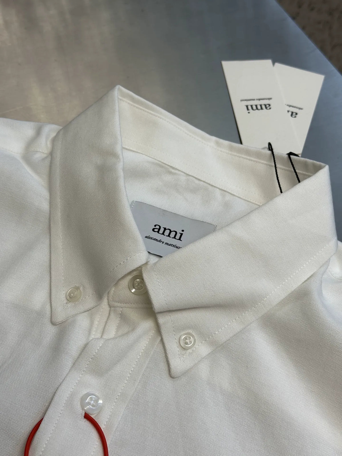 White button-up collar and placket with hanging tag marked 'ami'