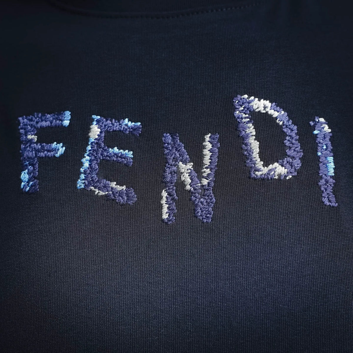 Close-up of embroidered FENDI lettering on navy crewneck T-shirt.