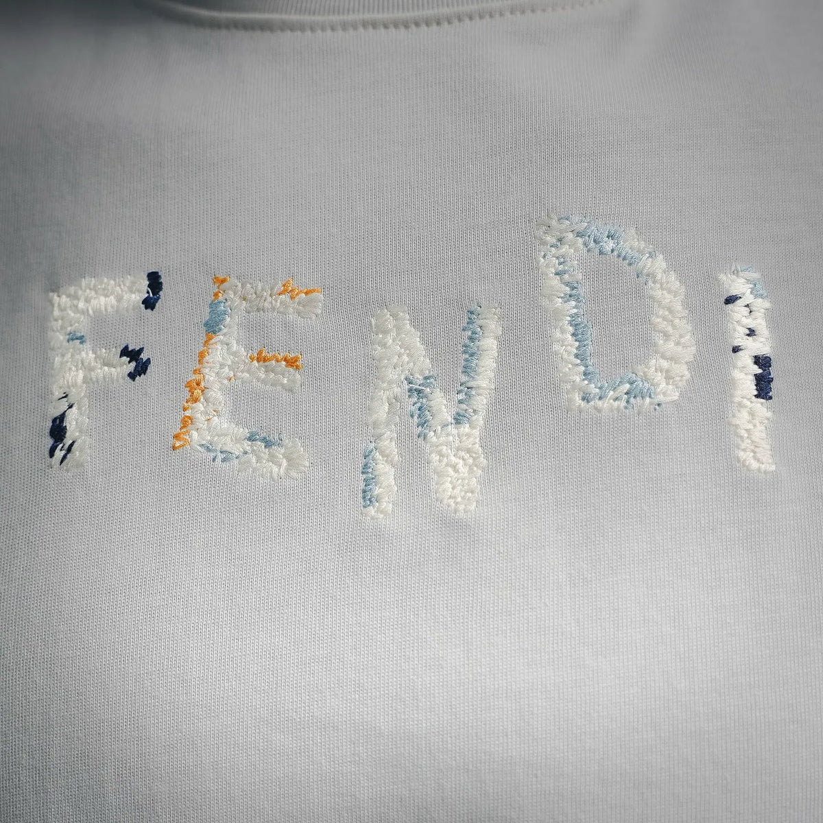 Close-up of embroidered graphic on white T-shirt with blue and orange stitching
